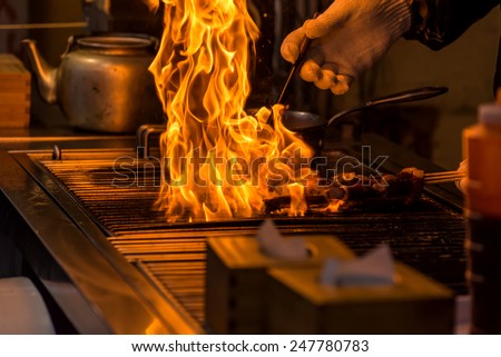 chef grilling bbq with flame of burning in restaurant.