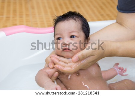 newborn baby taking a bath by mother at home, asian child.