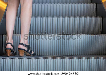 Business woman in high heels standing on escalators stairway.