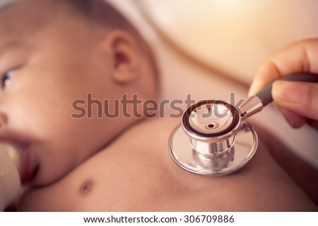 Pediatric doctor exams newborn baby girl with stethoscope in hospital.