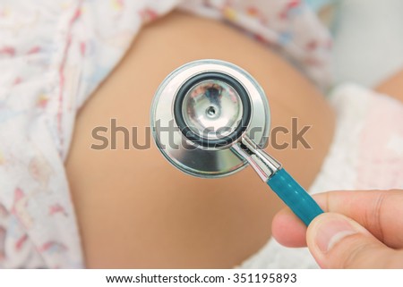 Pediatric doctor exams newborn baby girl with stethoscope in hospital.