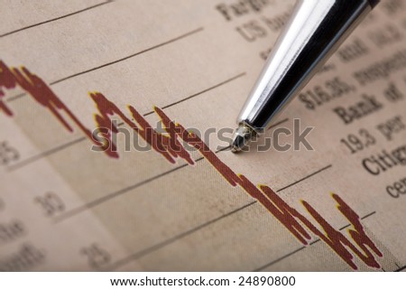 Analysis of a stock chart printed in a financial newspaper. Pen tip pointing at a declining red line graph.