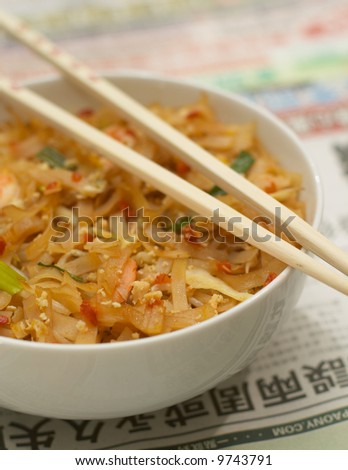 Bowl of chinese food with chopsticks on asian newspaper