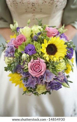 Bride holding colorful wedding bouquet of roses and sunflowers
