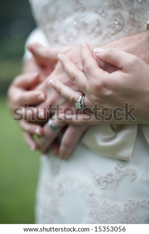 Bride and groom hands over wedding dress, focus on diamond ring