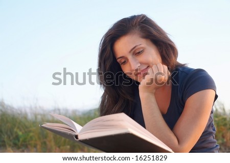 Pretty young woman reading a book outside