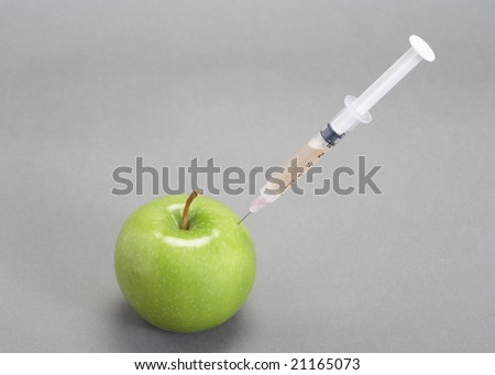 Syringe needle injected into green apple on grey
