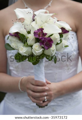 stock photo Bride holding white and purple wedding bouquet against gown