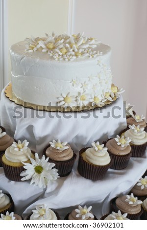White wedding cake with cupcakes at reception table