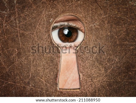 Man's eye looking through a keyhole antique door closeup