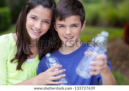 Smiling caucasian boy and girl holding up clear water bottles outside in yard,  for recycling