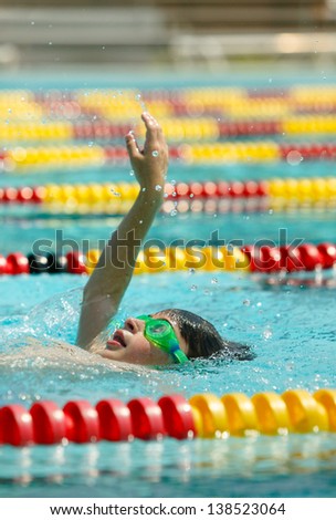 Caucasian Boy practices his backstroke swimming in lap pool with red and yellow lane markers.