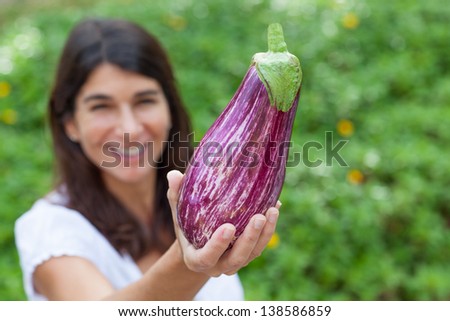 Tight shot of eggplant being held by Caucasian female hands of green foliage background.