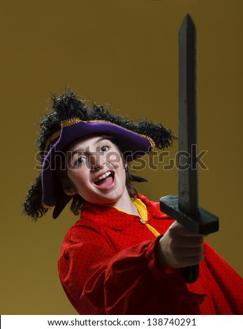 Young caucasian Boy with large purple pirate hat, red shirt and gray sword. Boy holds sword in the air yelling happily.