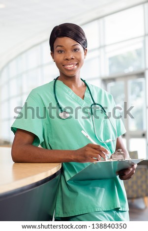 Smiling African American nurse at hospital work station lit brightly with clipboard and stethoscope.