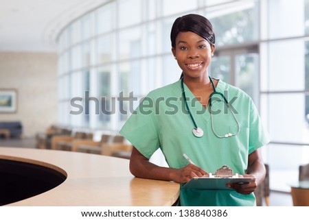 Smiling African American nurse at hospital work station lit brightly with clipboard and stethoscope.