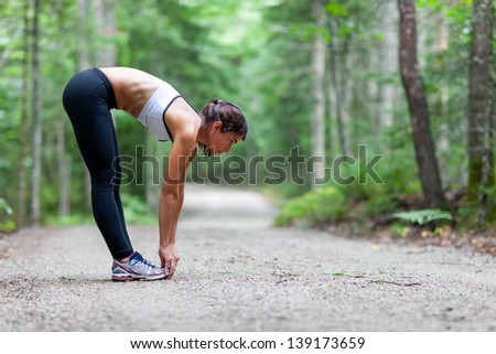 Middle Aged Woman Stretching In The Woods On A Dirt Road Before A Run