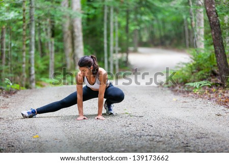 Middle aged woman stretching in the woods on a dirt road before a run