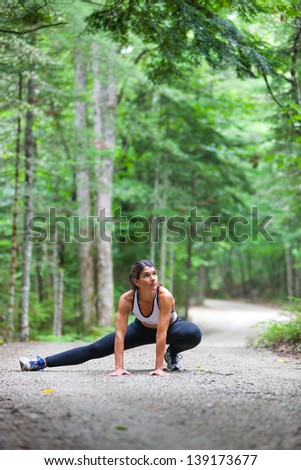 Middle aged woman stretching in the woods on a dirt road before a run