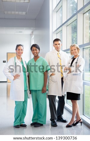 group of female and male doctors and nurses (Caucasian, African American, Hispanic ethnicity) smiling in lab coats and scrubs, in hospital looking at camera