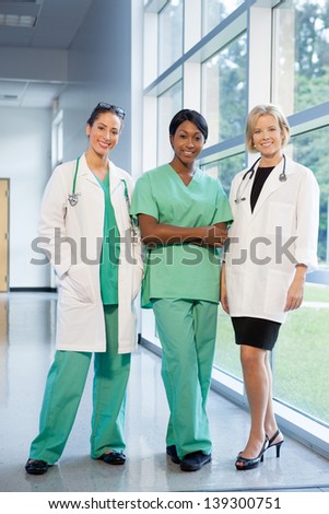 group of female doctors and nurses (Caucasian, African American, Hispanic ethnicity) smiling in lab coats and scrubs, in hospital looking at camera
