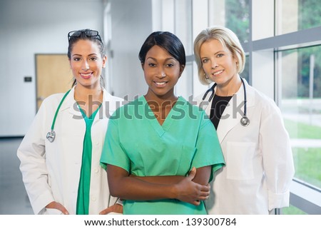 group of female doctors and nurses (Caucasian, African American, Hispanic) smiling in lab coats and scrubs, in hospital looking at camera
