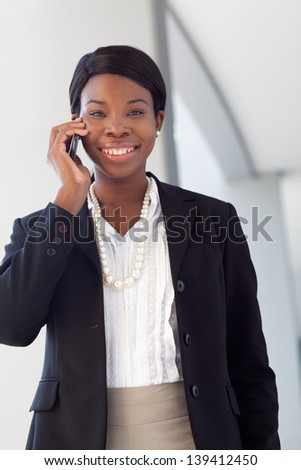 African-american business woman on cell phone, smiling, talking, in suit and pearls outside a modern building.