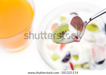 Spoon of yogurt with mixed fruits over dessert background (glass bowl filled with yogurt mixed with fruit pieces and glass of orange juice).