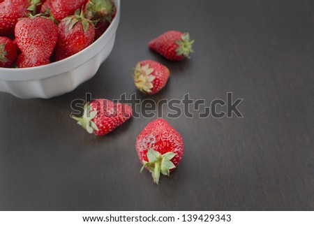 Small white bowl filled with succulent juicy fresh ripe red strawberries on an old wooden textured table top. Selective focus.
