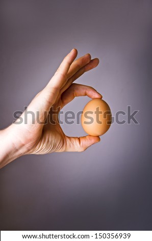Human hand holding a fresh egg on dark background