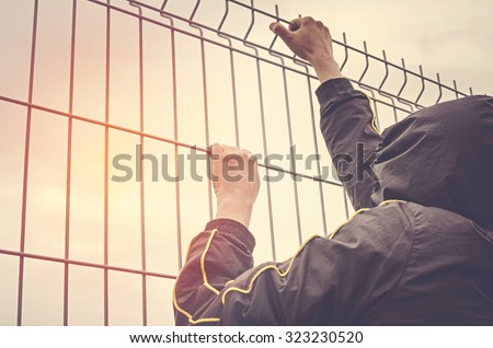 Refugee men and metal fence. Refugee crisis concept.