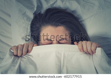 Woman with stressed face expression eyes closed hiding behind sheet in bed. \
The concept of avoiding responsibility.