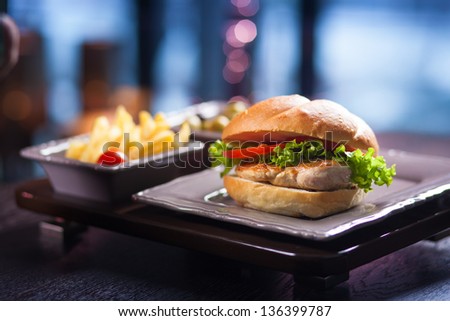 Color image. Burger shot with shallow focus on front with French fries and salad in background. Shooting in poor conditions. Developed from RAW;
