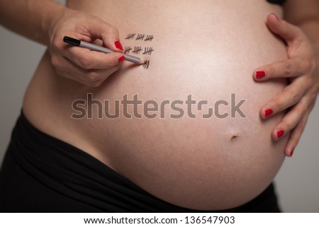 Pregnant woman writes a week during pregnancy on its belly with Tally Mark signs. Chubby body, and the red lacquer on hand. Shallow DOF. Developed from RAW; retouched with special care and attention.
