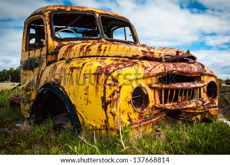 Abandoned yellow pickup truck rusting in a field.