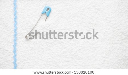 Blue safety pin and blue ribbon border on a white toweling background