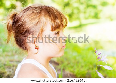 Close-up profile portrait of beautiful little girl, against green of summer park