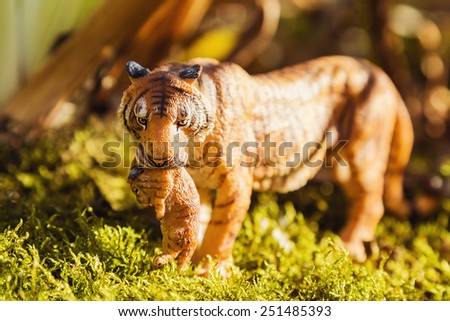 Tigress with a baby between her teeth. Tiger toy figurine in situation on defocused nature background.