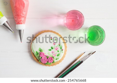 White icing cookie with painted roses on white background and cornets with glaze for painting