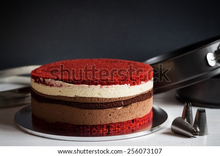 Naked layer cake with red velvet and chocolate biscuit and cream mousses on dark background with kitchen utensils