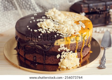 Romantic cake with chocolate glaze, cream flowers and  mango passion fruit mousse on retro background, \
vintage stylized photo