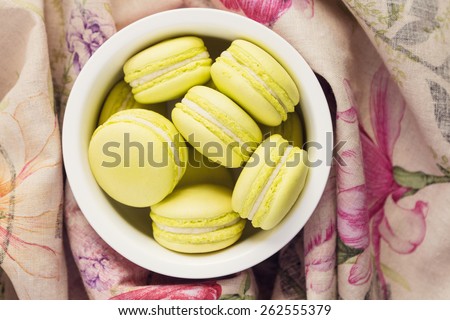 Top view of green macaroons in a bowl wrapped in floral cloth. Spring composition on pastel color, shallow focus