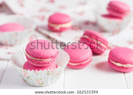 Some pink raspberry macaroons with floral paper cup on white shabby chic wooden background. Pastel colored composition with selective focus