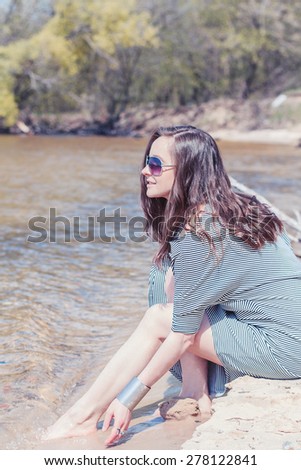 Beautiful young woman in sailor striped dress sits at the sand near water