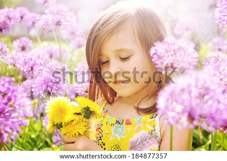 Little girl with dandelions, near Purple Flowers on a sunny day