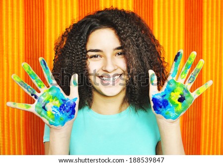 Pretty Latino American young girl with painted hands like a map of the earth on the background of bright orange stripes.   Happy girl with painted hands.