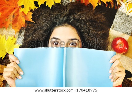 Latino American young girl lying on the dry leaves  reading a book with eyes wide open. Reading Book.