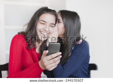 Two young woman discuss something. One from them whispers  something to other girl, who holds in her hand phone. Focus of a smart phone