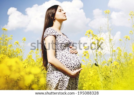 Pregnancy. Beautiful pregnant woman in blue dress enjoying free time in yellow rape field.