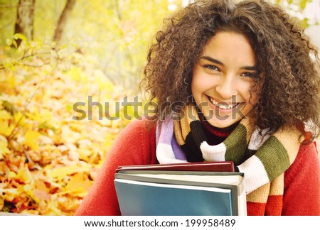 Female student in warm autumn. A smiling cute young female student with books in hand on the background of the autumn landscape